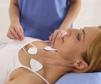 Doctor attaching ECG electrodes to patient's chest in clinic, closeup