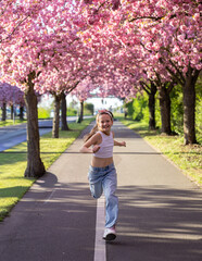 Obraz premium Happy girl running under blooming cherry blossom trees on sunny spring avenue