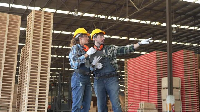Workers discuss tasks and safety in a large warehouse with wooden pallets during the day