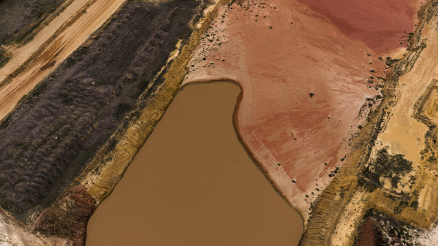 Aerial view of industrial salt mining patterns with brown and yellow sediment-filled pools, textured sand, and earthworks in the landscape in Kalbarri, Western Australia, Australia.