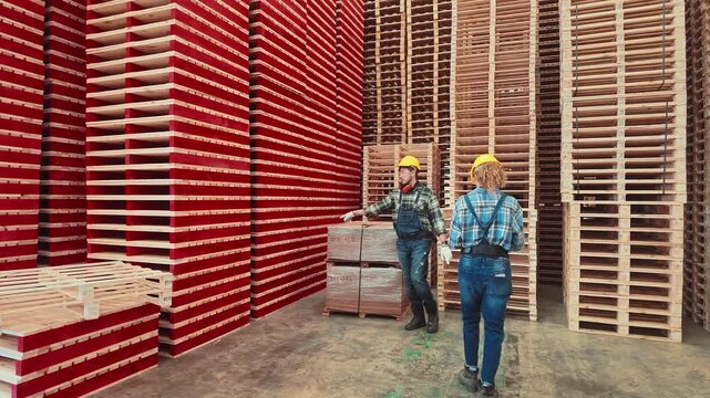 Workers inspect wooden pallets in a warehouse in the afternoon under bright lights