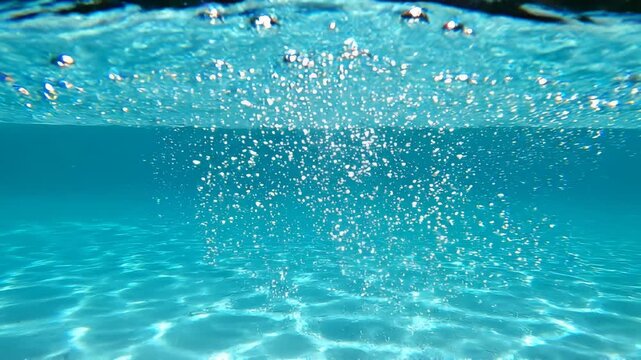 Bubbles rising through clear turquoise water with sunlight patterns on sandy seabed cinematic