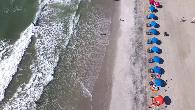 Blue umbrellas form a row beside breaking surf in an overhead Myrtle Beach view.
