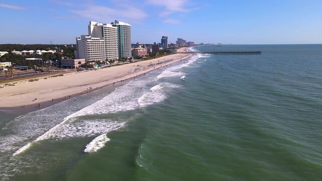 Breaking waves lead beside South Carolina resort towers beneath a moving coastal panorama.
