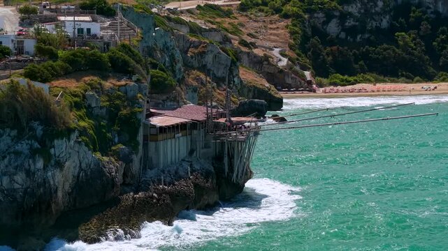 Telephoto aerial close up of Trabucco da Elia wooden beams with crashing sea waves and Zaiana beach background in Peschici Gargano Puglia Italy cinematic drone B-roll