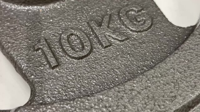 Close-up of a grey textured ten kilogram cast iron weight plate. Fitness equipment, bodybuilding gym training concept, heavy steel barbell disk details.