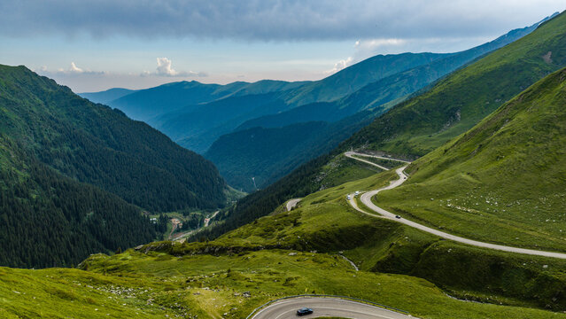Aerial view of the winding Transfagarasan mountain pass with lush green slopes and cars driving along the road in Curtea de Arges, Judetul Arges, Romania.