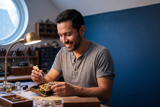 Hispanic man smiling while repairing a vintage clock at a workbench