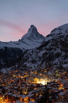 Zermatt village illuminated at dusk with snow covered Matterhorn peak in winter