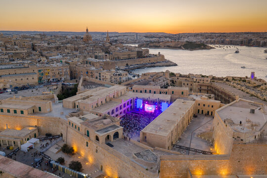 Aerial view of a concert taking place in the courtyard of Fort St. Elmo with blue stage lights, surrounded by historic limestone walls at sunset in Valletta, Port Region, Malta.