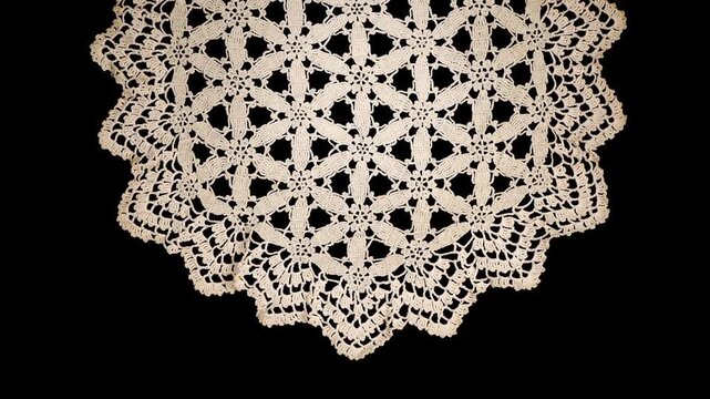 Round crochet beige doily lace isolated on black background, crocheted Grandma's doily, detail of handmade embroidery, tablecloth, napkin, vintage art design. Craft linen. Flat lay, top view, rotating