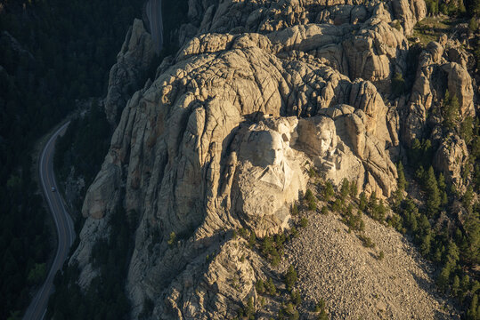 Aerial view of Mount Rushmore National Memorial featuring carved granite presidential faces, surrounded by pine forests and a winding road in Keystone, South Dakota, United States.