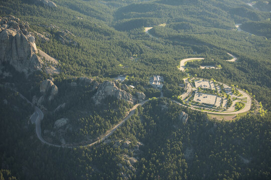 Aerial view of Mount Rushmore National Memorial surrounded by dense pine forests, winding roads, and parking facilities in Keystone, South Dakota, United States.
