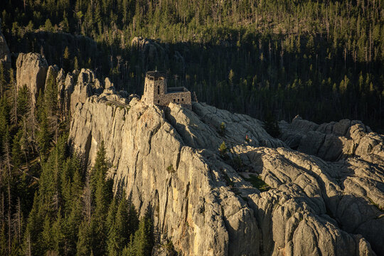 Aerial view of the historic stone fire tower atop Black Elk Peak surrounded by rugged granite rock formations and dense pine forests in Keystone, South Dakota, United States.