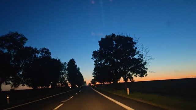 Oncoming headlights on a rural road beneath a twilight sky