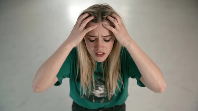 Young woman Aggressively running hands backward through the hair, gripping it tightly at the back of the head.