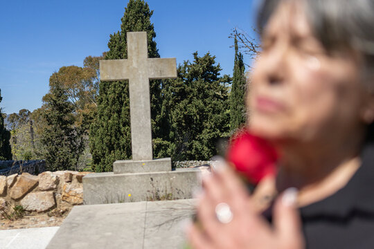unrecognizable woman crying  in a sacred cemetery christian cross . Holding a red rose and praying in a family   burial.
