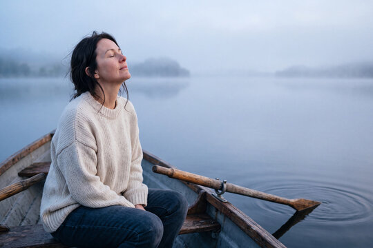 Mature woman finding peace in a rowboat on a misty lake
