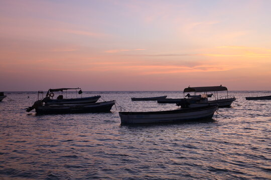 Scenic view of small fishing boat silhouettes floating on calm sea during colorful sunset or dusk, ideal for travel, leisure, and nature - colorful sky