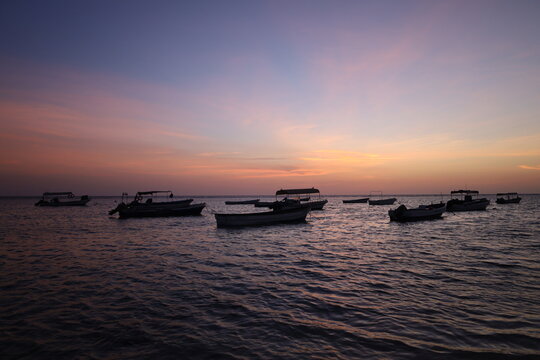 Scenic view of small fishing boat silhouettes floating on calm sea during colorful sunset or dusk, ideal for travel, leisure, and nature - colorful sky