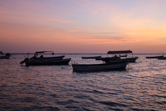 Scenic view of small fishing boat silhouettes floating on calm sea during colorful sunset or dusk, ideal for travel, leisure, and nature - colorful sky
