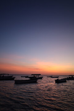 Scenic view of small fishing boat silhouettes floating on calm sea during colorful sunset or dusk, ideal for travel, leisure, and nature - colorful sky