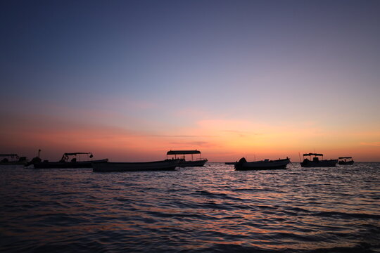 Scenic view of small fishing boat silhouettes floating on calm sea during colorful sunset or dusk, ideal for travel, leisure, and nature - colorful sky