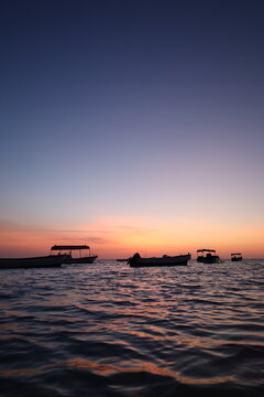 Scenic view of small fishing boat silhouettes floating on calm sea during colorful sunset or dusk, ideal for travel, leisure, and nature - colorful sky