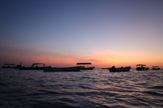 Scenic view of small fishing boat silhouettes floating on calm sea during colorful sunset or dusk, ideal for travel, leisure, and nature - colorful sky