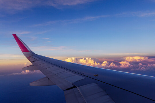 Vista de janela de avi&atilde;o da asa sobrevoando nuvens ao p&ocirc;r do sol durante voo comercial
