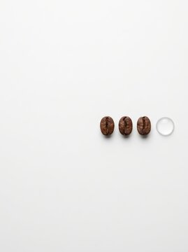 Three roasted coffee beans in a row with a single water drop on white background. Minimalist flat lay with large copy space. Coffee brewing and dilution concept. Menu, packaging, branding.