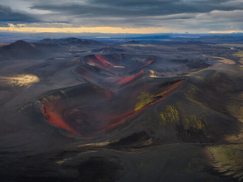 Aerial view of the volcanic craters in the Highlands with dark volcanic soil and vibrant mossy patches under a dramatic cloudy sky in Iceland.