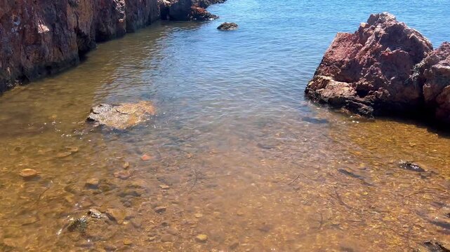 Clear golden water gently lapping between rugged red rocks in a secluded shallow cove along the Ayvalik, Ortunc Bay.