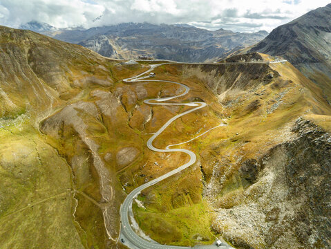 Aerial view of Grossglockner High Alpine Road winding through the rugged alpine landscape with rocky slopes and mountain peaks under a cloudy sky, Zell am See District, Salzburg, Austria.