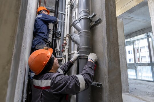 Workers install plumbing systems in a building under construction during the day