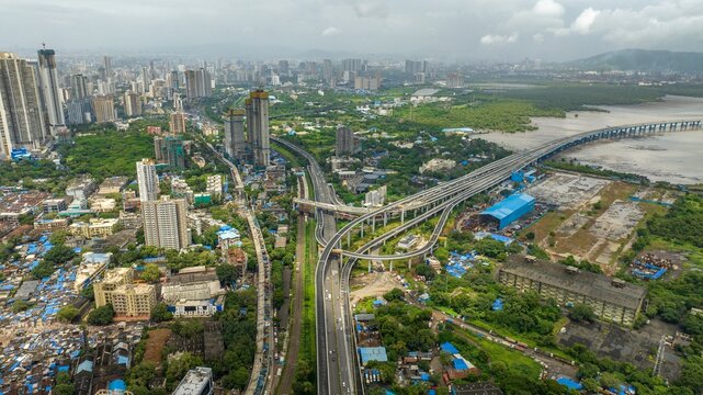 Aerial view of Atal Bihari Vajpayee Sewri-Nhava Sheva Atal Setu bridge spanning the bay with highway infrastructure, urban cityscape, and greenery in Mumbai, Maharashtra, India.