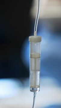 Intravenous infusion drip chamber with saline solution and bubbles in operating room, medical IV line close-up with copy space