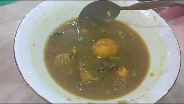 Indonesian soto daging, traditional beef soup with broth, meat chunks and young chicken egg yolk telur muda served in white bowl in warung