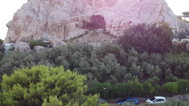 Aerial view of the rocky Acropolis hill surrounded by lush olive trees and Mediterranean vegetation in Athens, Greece.