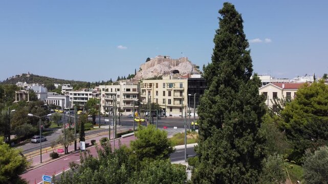 Aerial view of the historic Acropolis of Athens rising above the urban landscape with a tall cypress tree in the foreground in Athens, Greece.