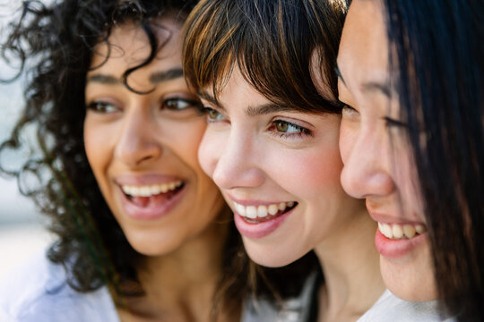 Close up portrait of young multiracial women friends smiling side by side outdoors. Friendship and travel concept.