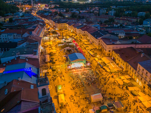 Aerial view of Radvansky jarmok traditional market at night with illuminated stalls, a central stage, and crowds in the historic square in Banska Bystrica, Banskobystricky kraj, Slovakia.