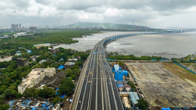 Aerial view of the Atal Bihari Vajpayee Sewri Nhava Sheva Atal Setu bridge stretching across the bay with surrounding urban landscape and coastal greenery in Mumbai, Maharashtra, India.