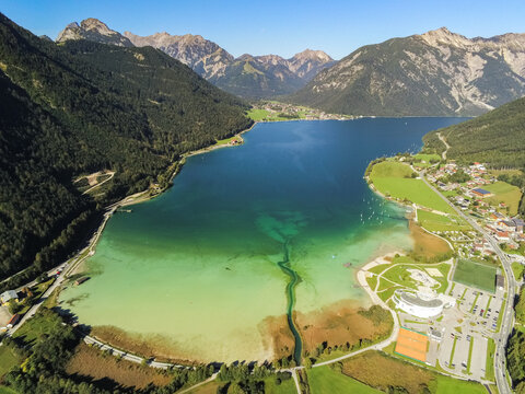 Aerial view of Achen Lake surrounded by lush green mountains and small villages in the Schwaz District, Tyrol, Austria.