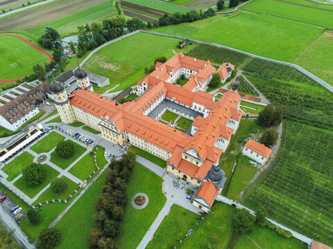 Aerial view of Stift Stams with its historic orange-tiled roofs and courtyard surrounded by lush green fields and gardens in Stams, Tirol, Austria.