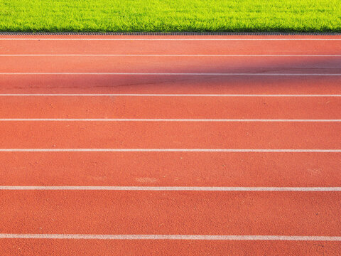 Red running track with white lane markings and green grass field alongside