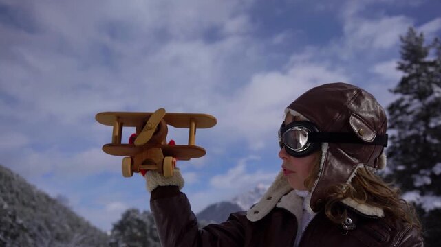 A happy child is playing with a wooden airplane outside in winter. A child with a toy airplane pretends to be a pilot. The concept of childhood dreams and freedom. Slow motion