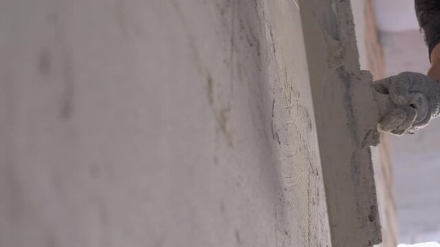 Worker smoothing plaster on wall with hand trowel during renovation