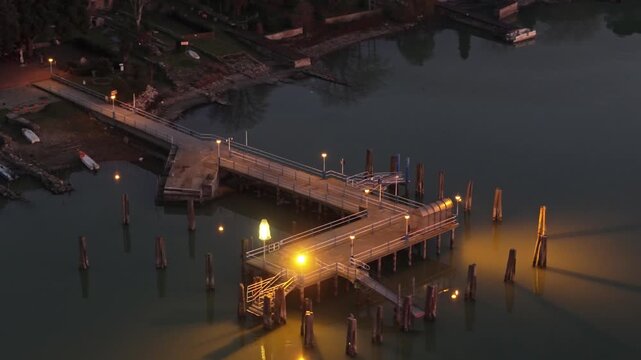 Aerial view of the illuminated wooden pier extending into Lake Trasimeno at Isola Maggiore, Tuoro sul Trasimeno, Umbria, Italy.