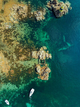 Aerial view of the lighthouse and rocky coastline with clear turquoise waters and small boats in Ile-de-Brehat, Brittany, France.